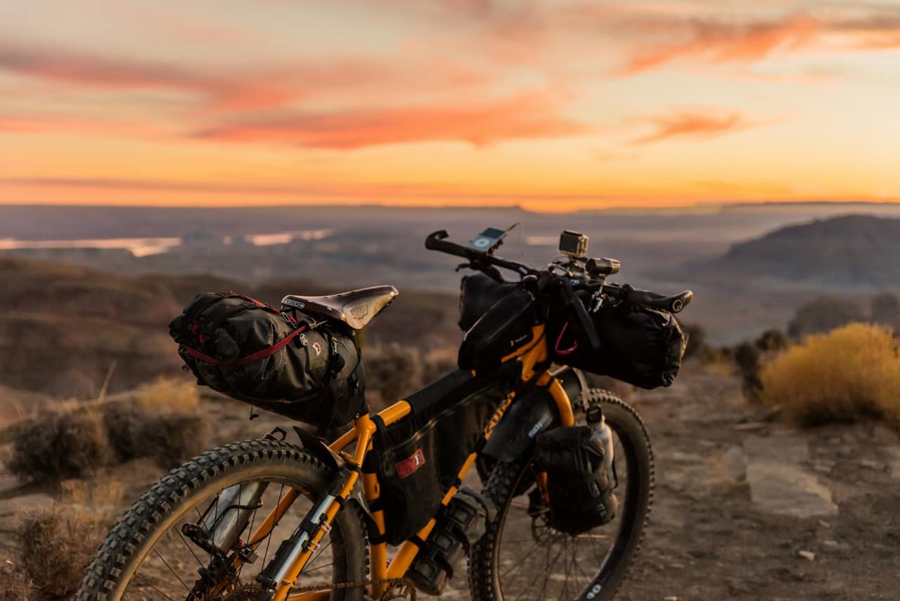 Loaded bicycle overlooking a canyon at dusk. Not a listed e-bike model. Shown with Ridstar as atmosphere, not as a photograph of that product.